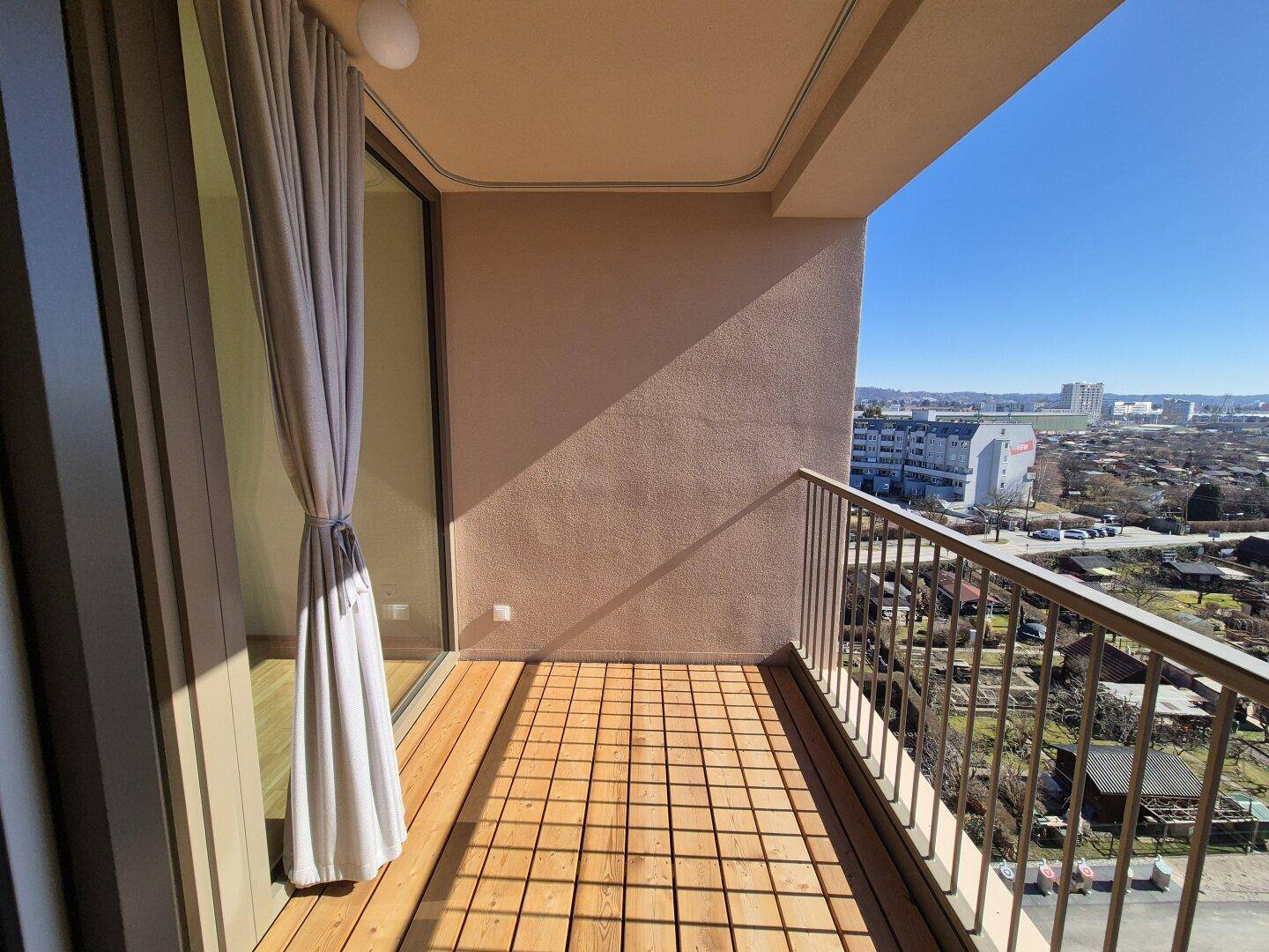 Sonniger Balkon mit Holzboden und weitem Blick über die Stadt und die umliegende Landschaft.
