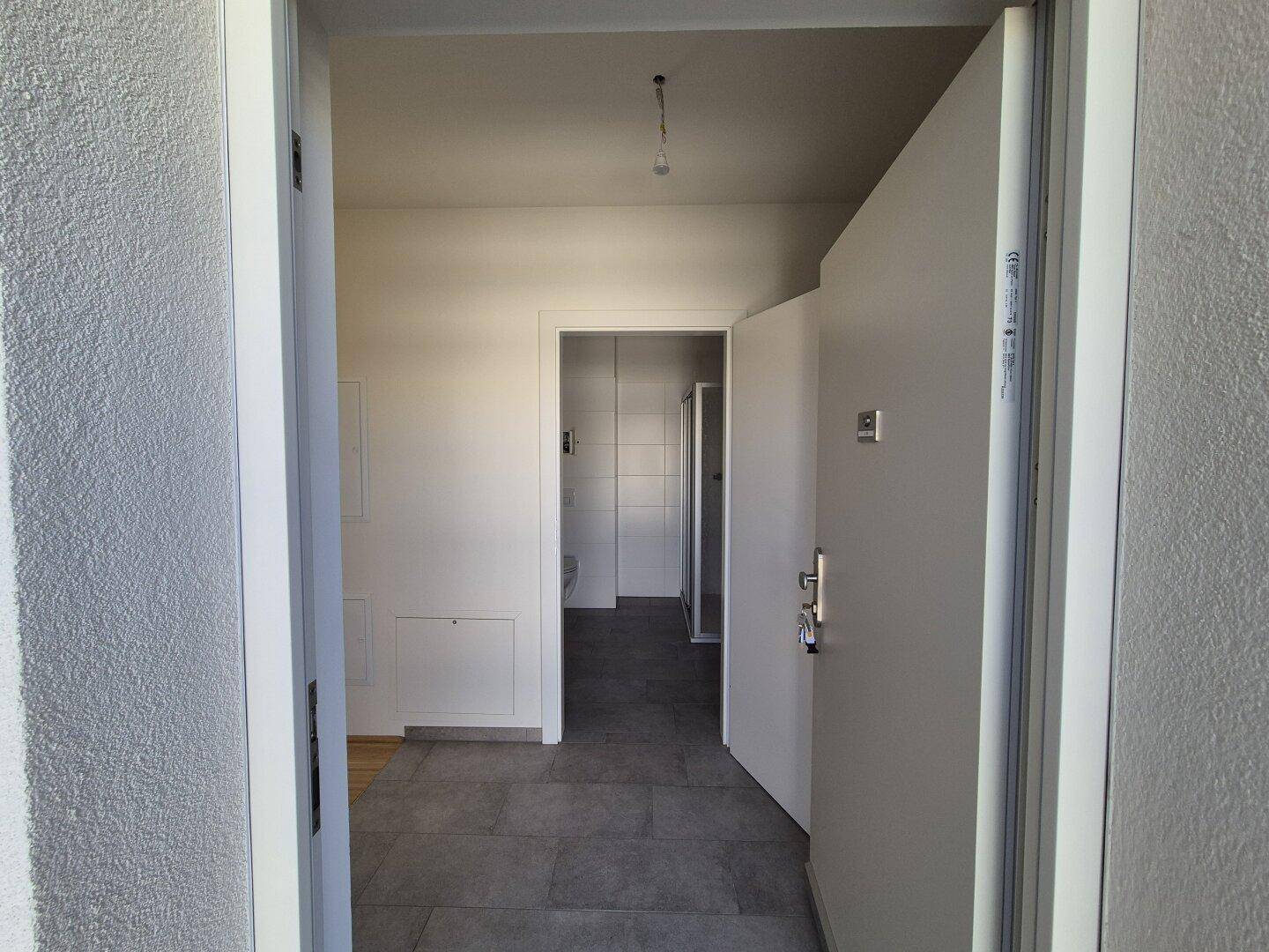 Heller Eingangsbereich mit grauen Fliesen und Blick in den Flur und das Badezimmer.