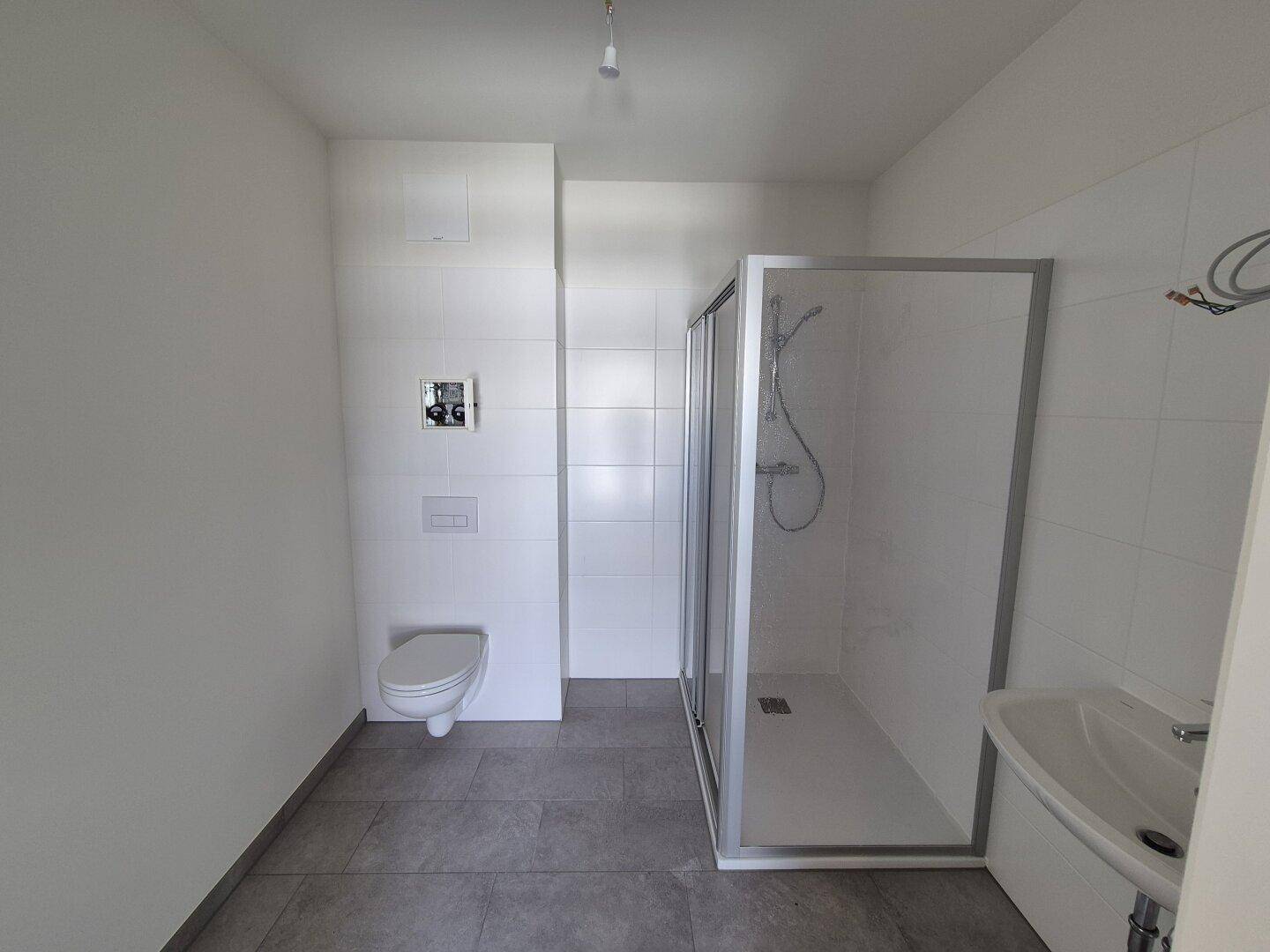 Modernes Badezimmer mit weißen Fliesen, wandhängendem WC und einer Duschkabine.