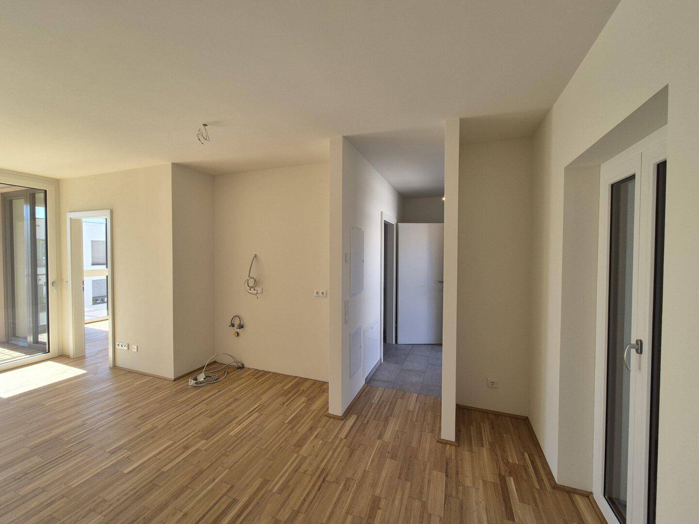 Offener Wohnbereich mit Holzboden und Zugang zu weiteren Räumen, hell und modern.
