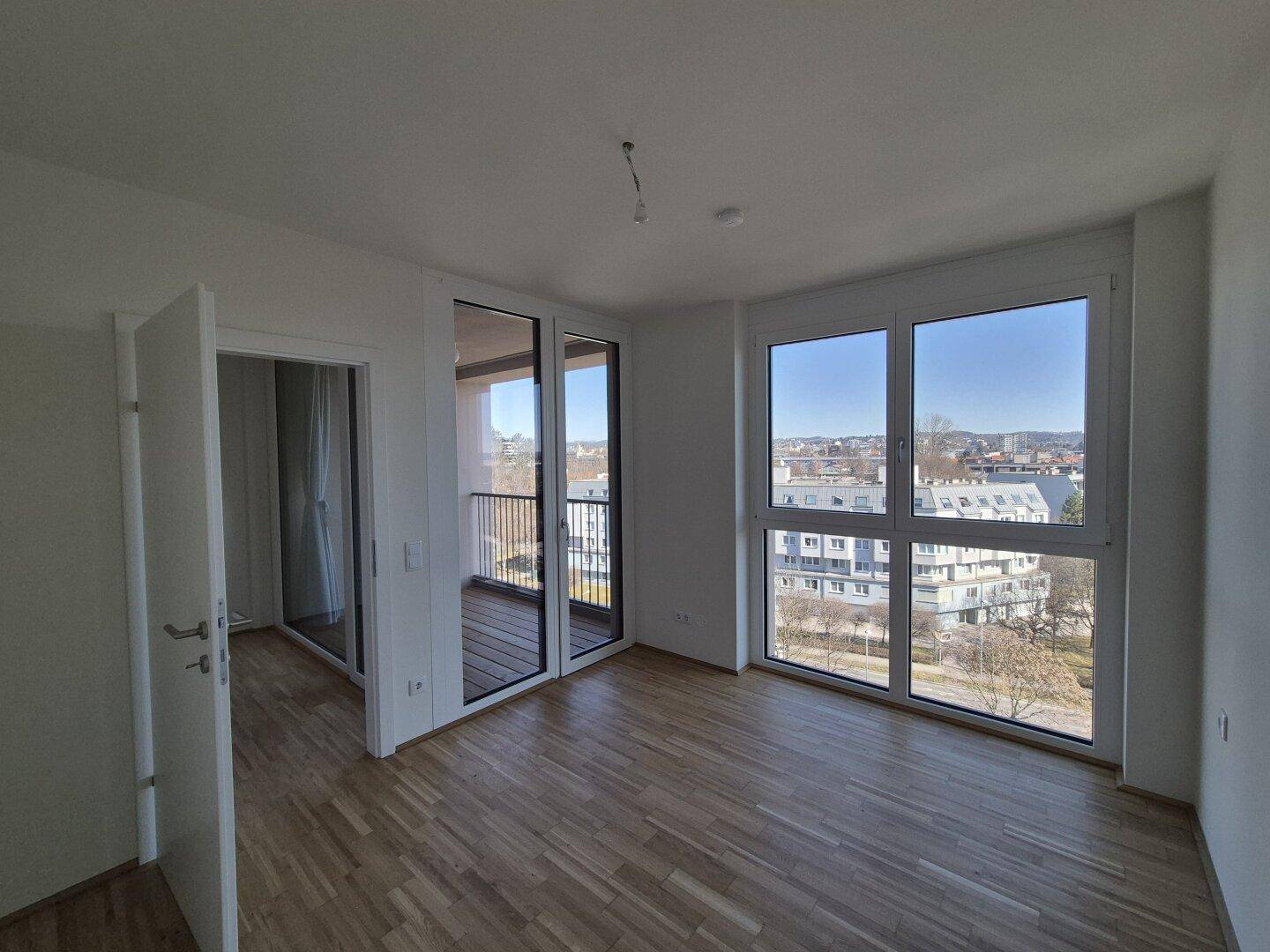 Heller Wohnraum mit Parkettboden, großen Fenstern und Balkonzugang, bietet Stadtblick.