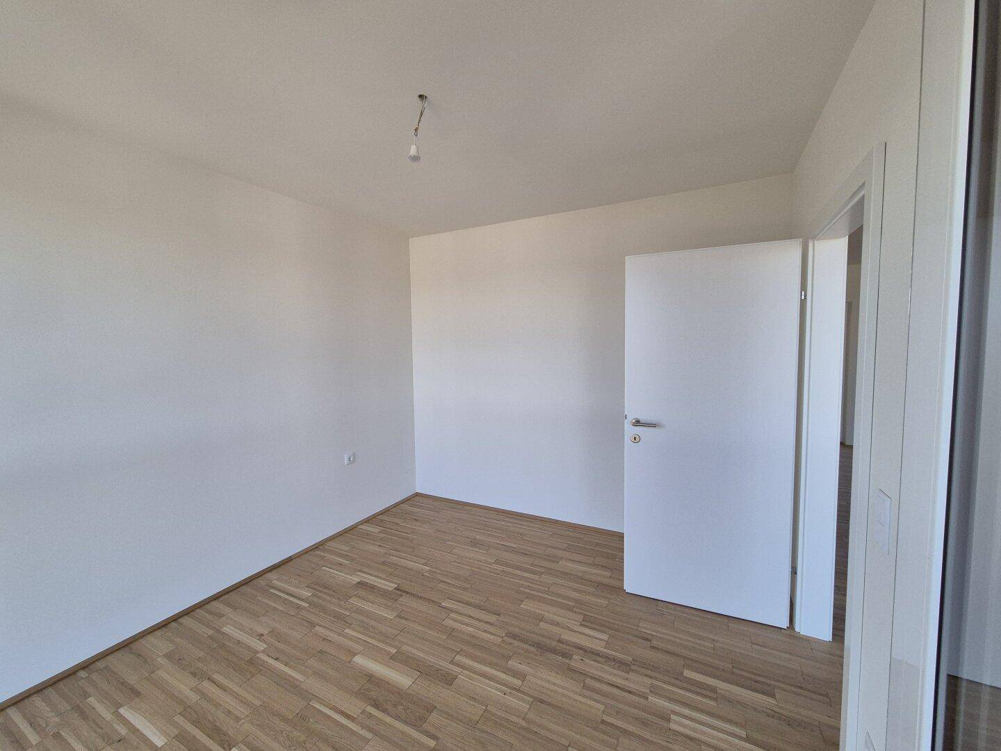 Ruhiges Schlafzimmer mit Parkettboden und weißen Wänden, ideal für persönliche Einrichtung.