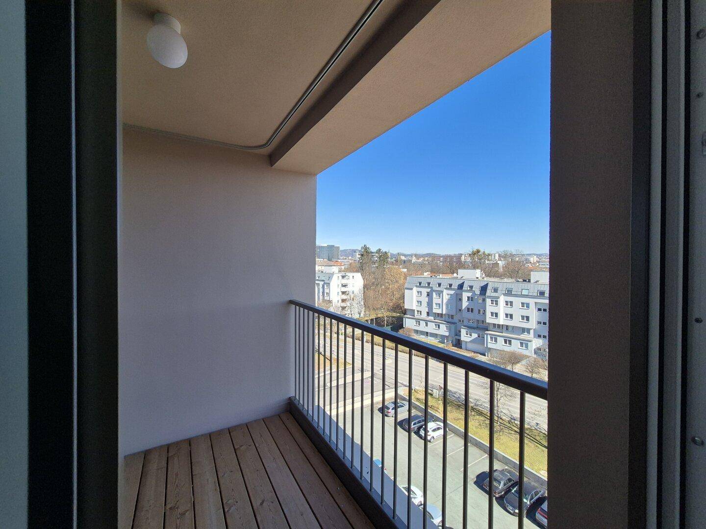 Sonniger Balkon mit Holzdielen und Blick auf die umliegende Stadtlandschaft.