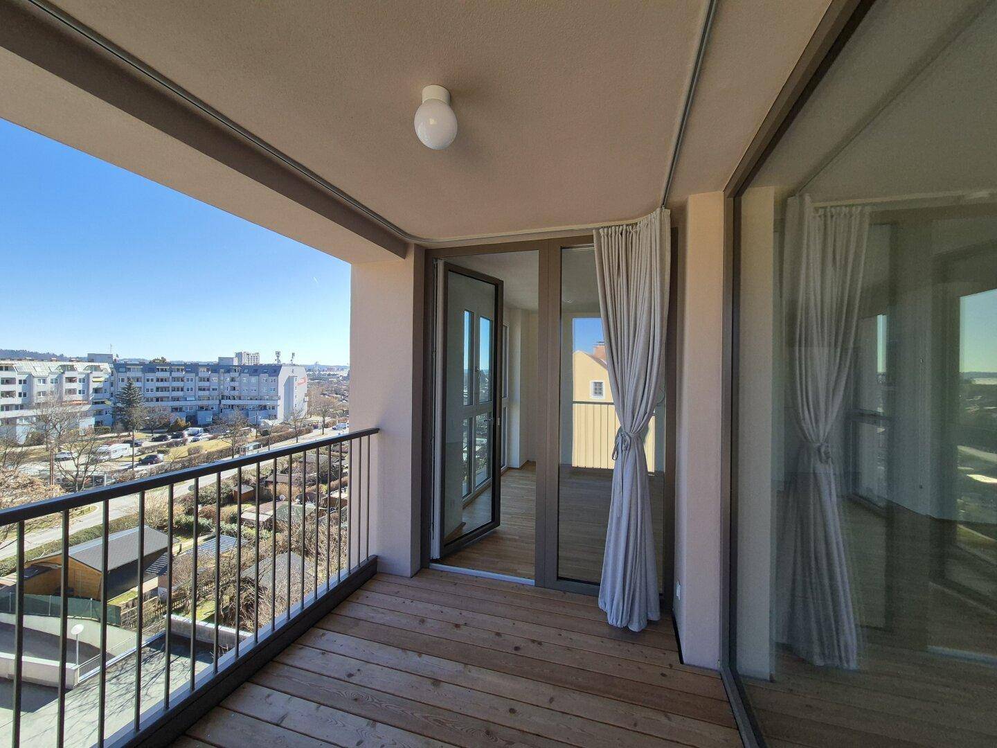 Sonniger Balkon mit Holzdielen und weitem Blick über die Stadt, ideal für Erholung im Freien.