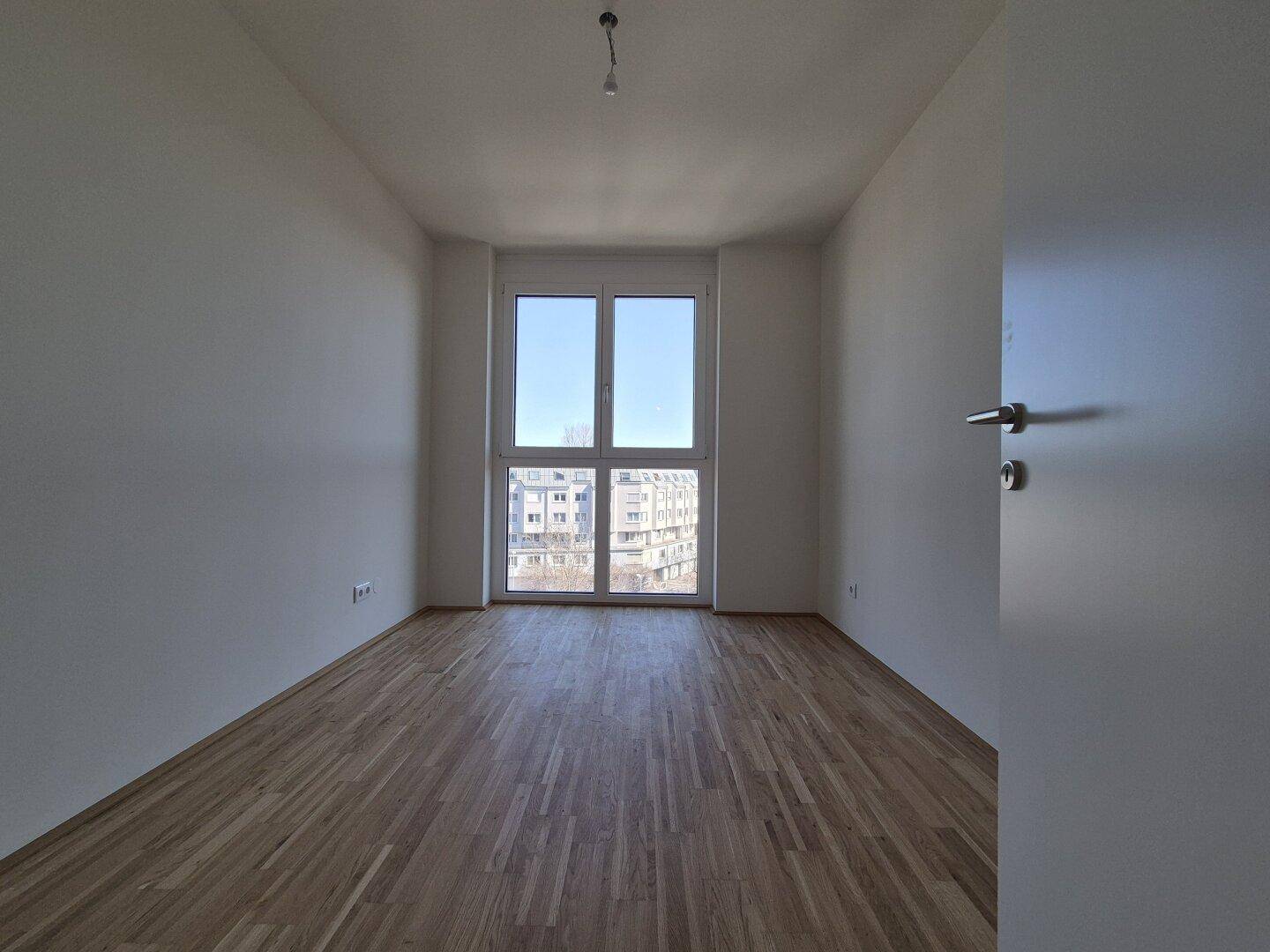 Lichtdurchflutetes Zimmer mit Parkettboden und großen Fenstern, bietet einen schönen Blick auf die Umgebung.