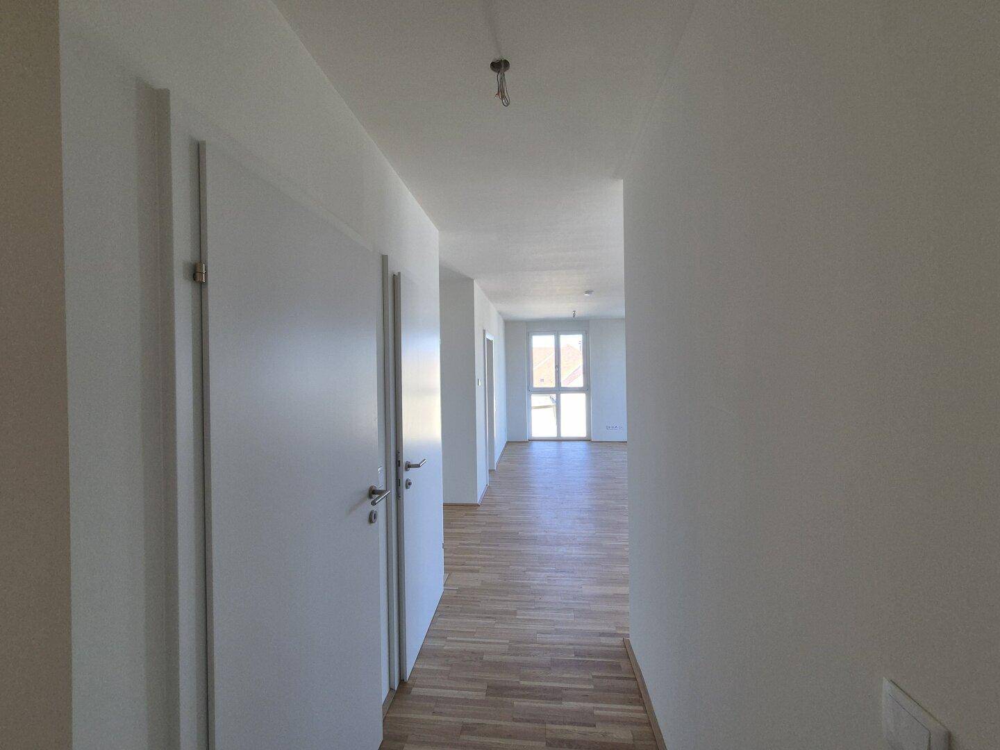 Heller Flur mit modernem Parkettboden und weißen Türen, der zu verschiedenen Räumen führt.
