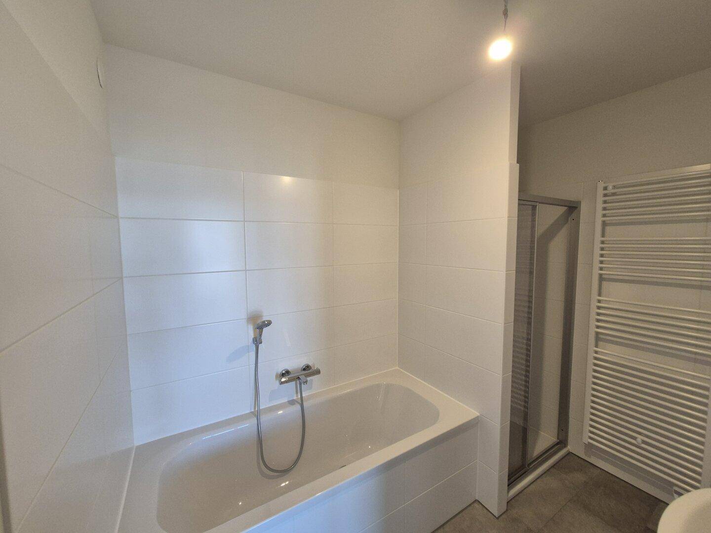 Modernes Badezimmer mit weiß gefliesten Wänden, Badewanne, Duschkabine und Handtuchheizkörper.