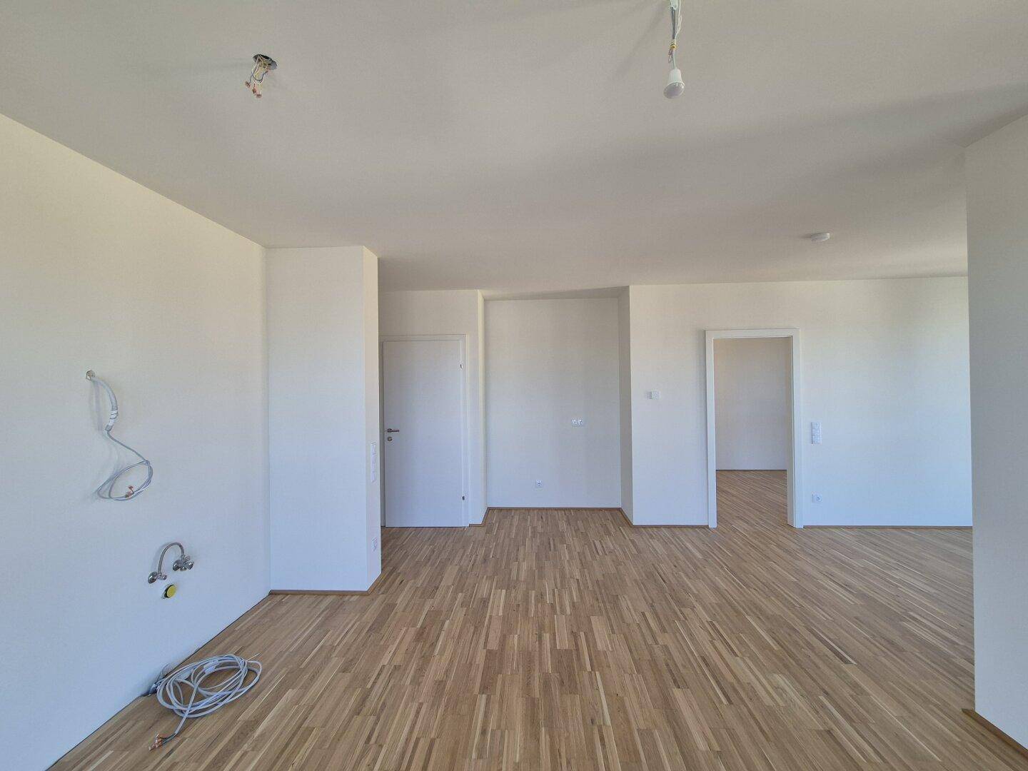 Offener Wohnbereich mit hellem Parkettboden und weißen Wänden, bietet vielseitige Gestaltungsmöglichkeiten.