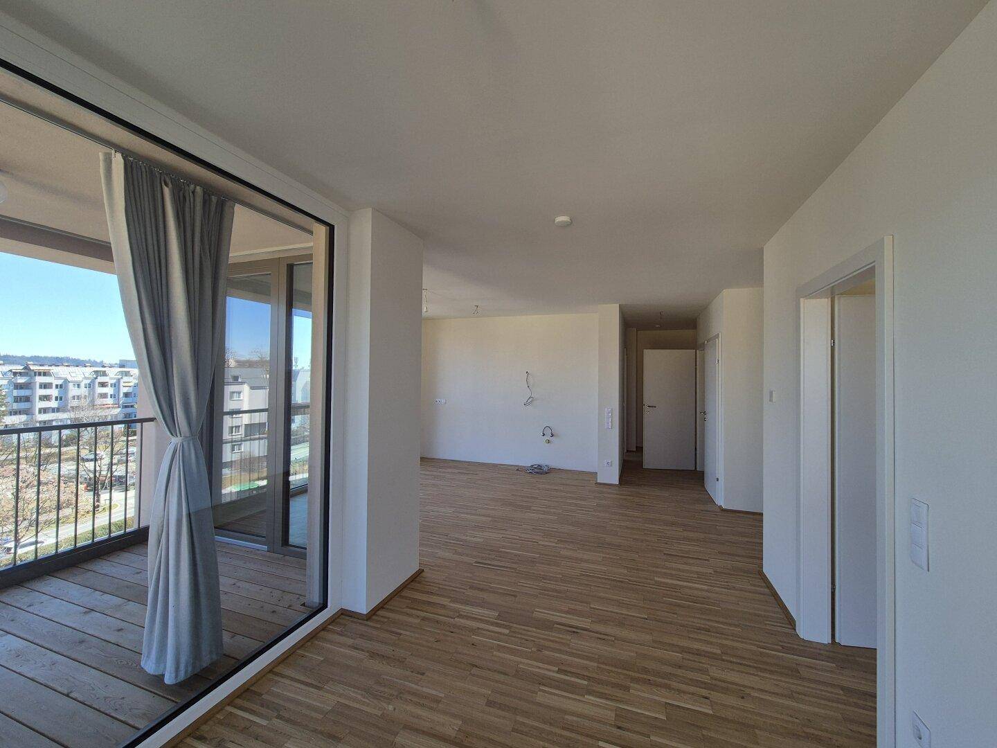 Geräumiger Wohnbereich mit Parkettboden und Zugang zu einem sonnigen Balkon mit Stadtblick.