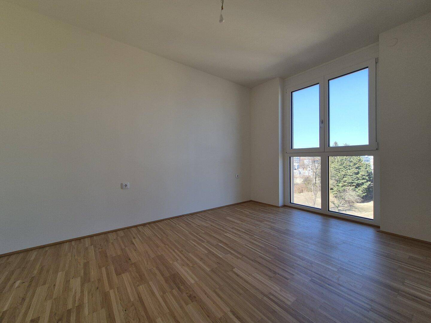Helles Schlafzimmer mit Parkettboden und großen Fenstern, bietet einen angenehmen Ausblick ins Grüne.