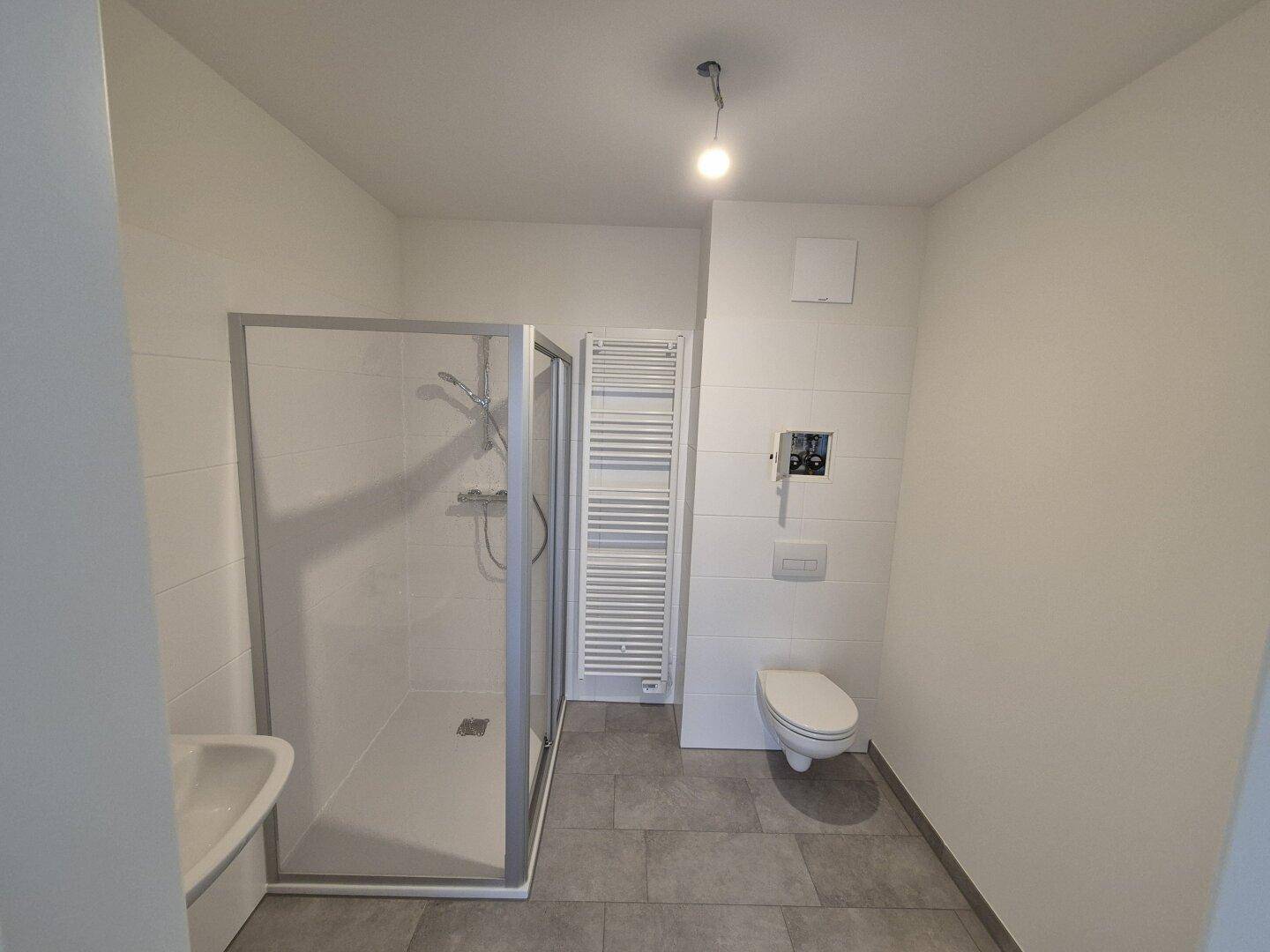 Modernes Badezimmer mit Dusche, Wand-WC, beheiztem Handtuchhalter und grauen Fliesen.