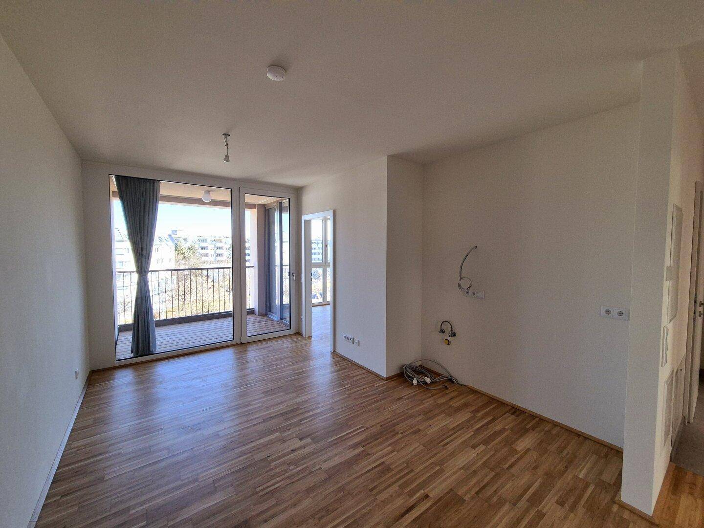 Geräumiger, heller Wohnraum mit Parkettboden und großen Fenstertüren zum Balkon.
