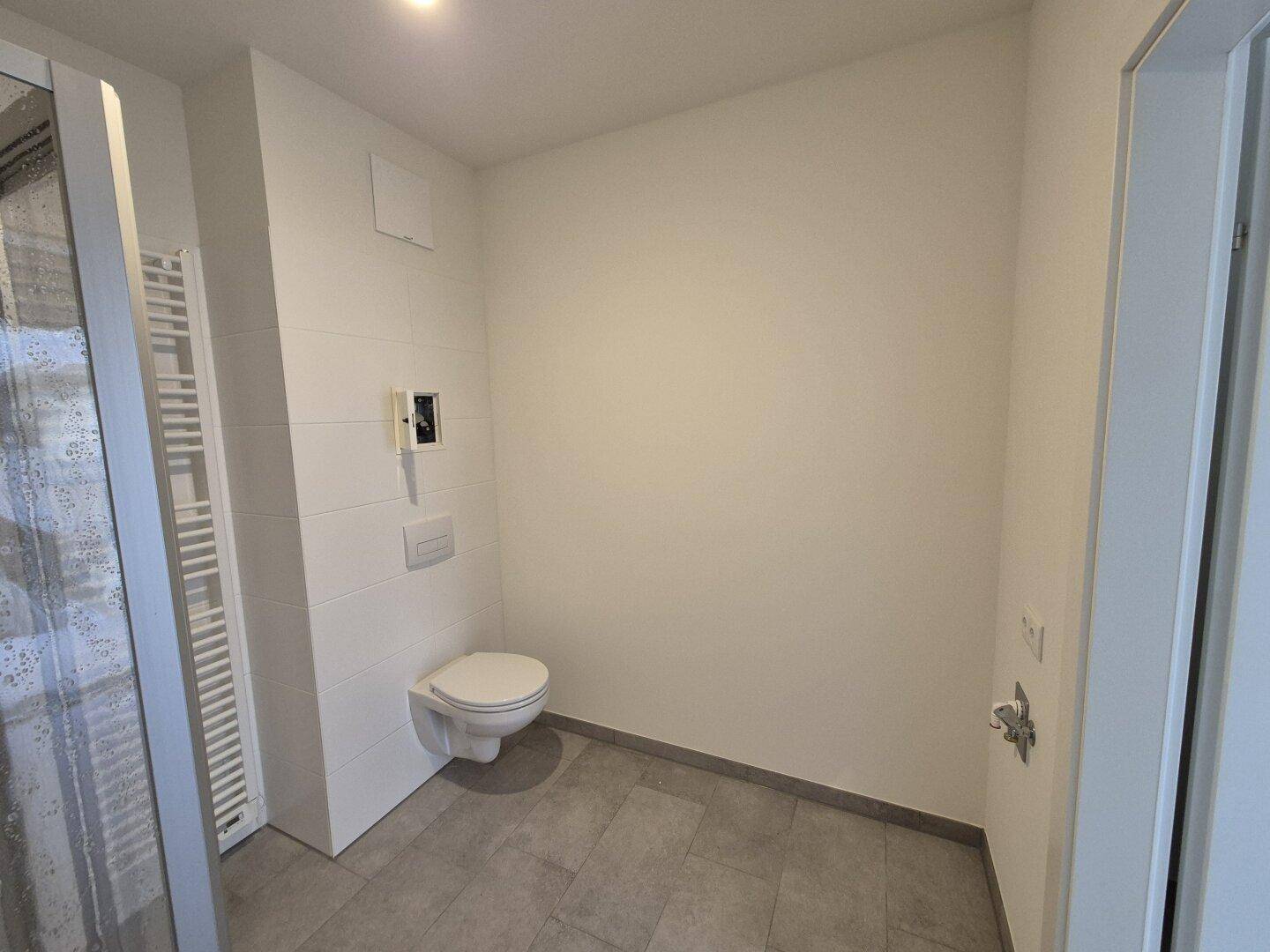 Helles Badezimmer mit wandhängendem WC, Fliesenboden und Heizkörper.