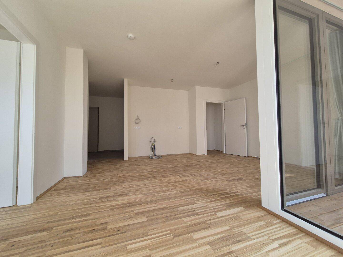Geräumiger, heller Innenraum mit Holzboden und mehreren Türen, bereit zur individuellen Gestaltung.