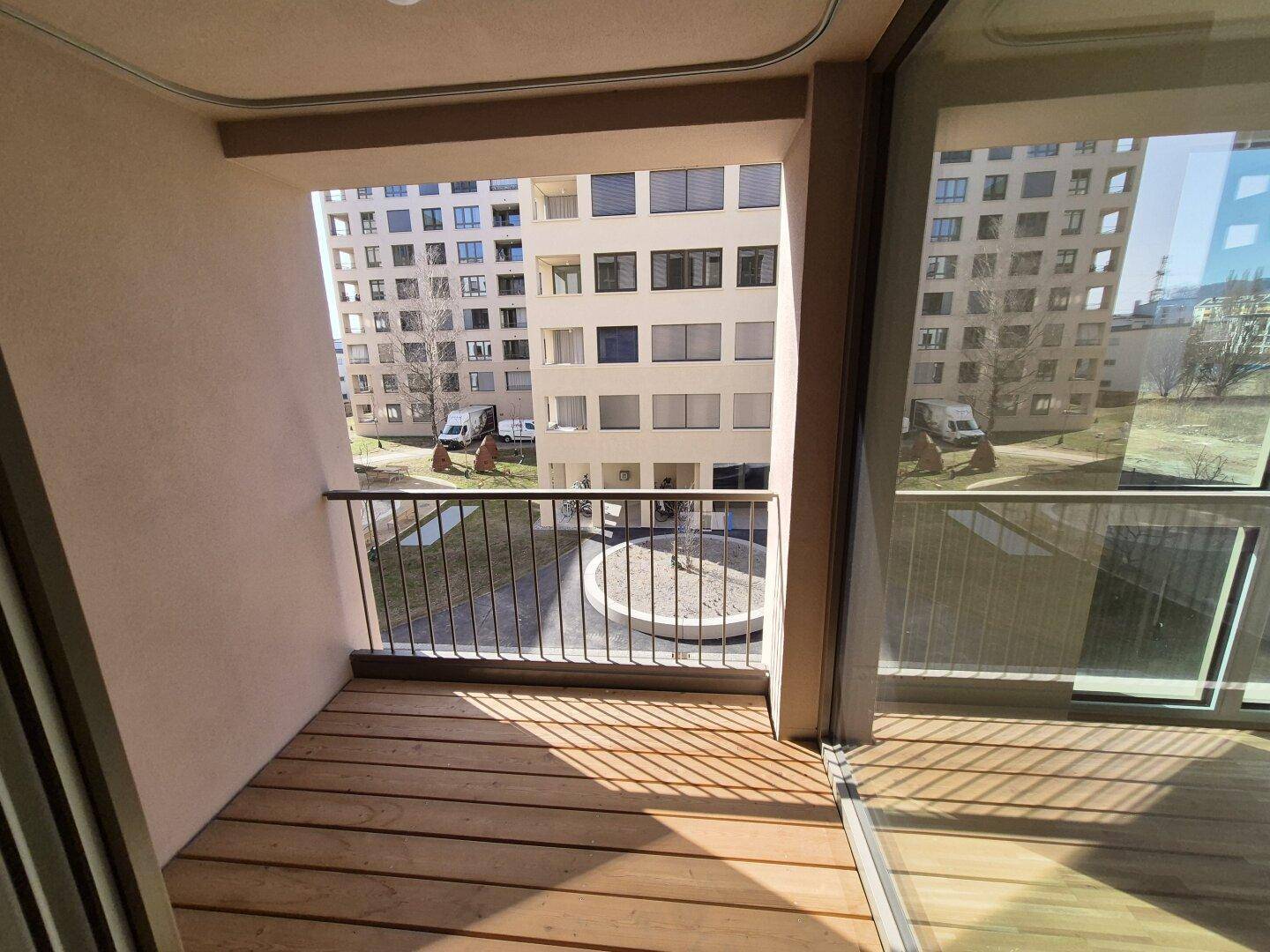 Kleiner Balkon mit Holzboden und Blick auf den begrünten Innenhof der Wohnanlage.