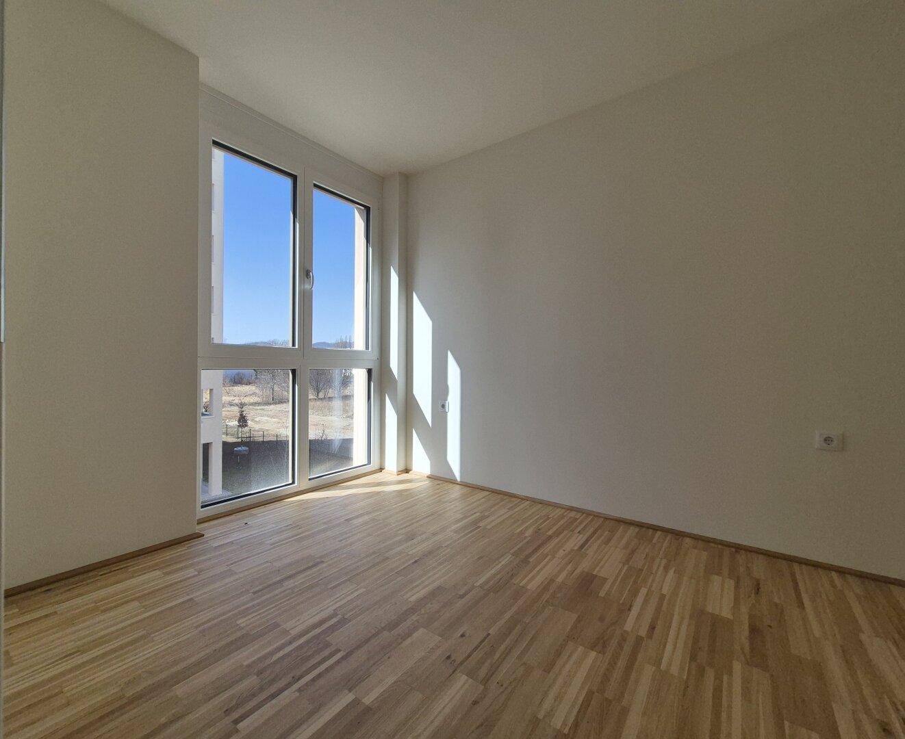 Helles Zimmer mit großen Fenstern und Holzboden, ideal als Schlaf- oder Arbeitszimmer.