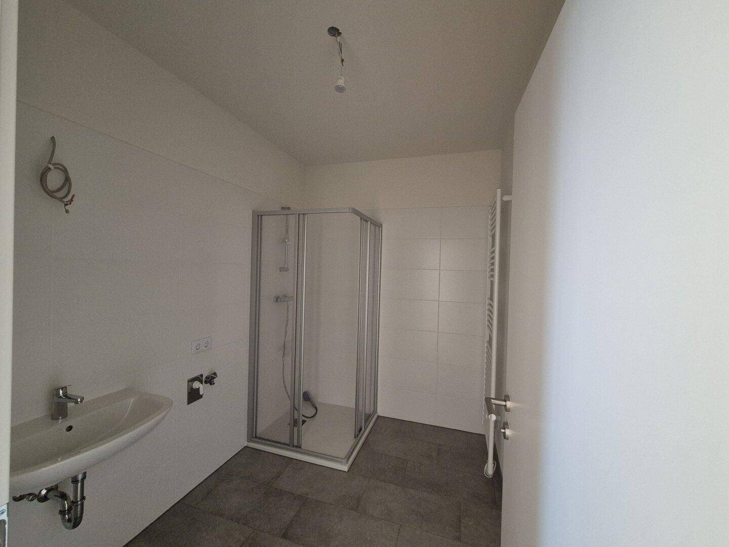 Modernes Badezimmer mit Dusche, Waschbecken und Handtuchheizkörper in hellen Fliesen.