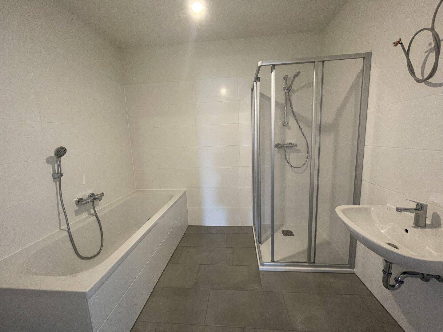 Modernes Badezimmer mit Badewanne, Duschkabine und Waschbecken in hellen Fliesen.
