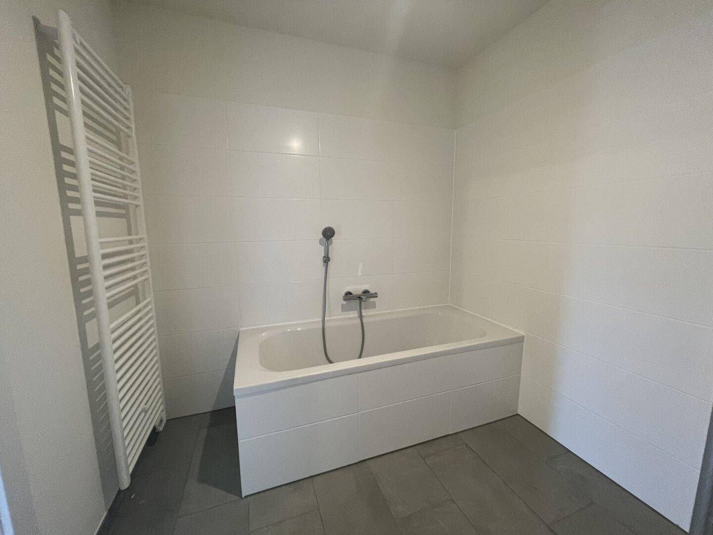 Badezimmer mit Badewanne, weißen Wandfliesen und einem beheizten Handtuchhalter.