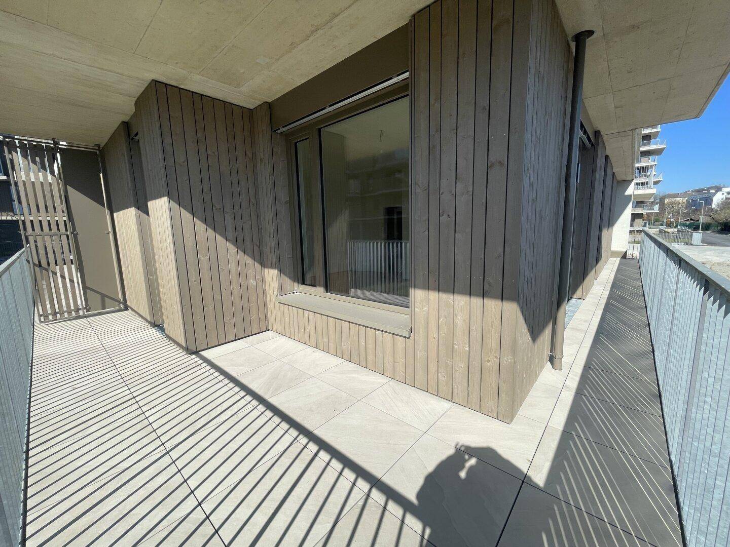Geräumiger Balkon mit Fliesenboden und Holzverkleidung an der Fassade des modernen Gebäudes.