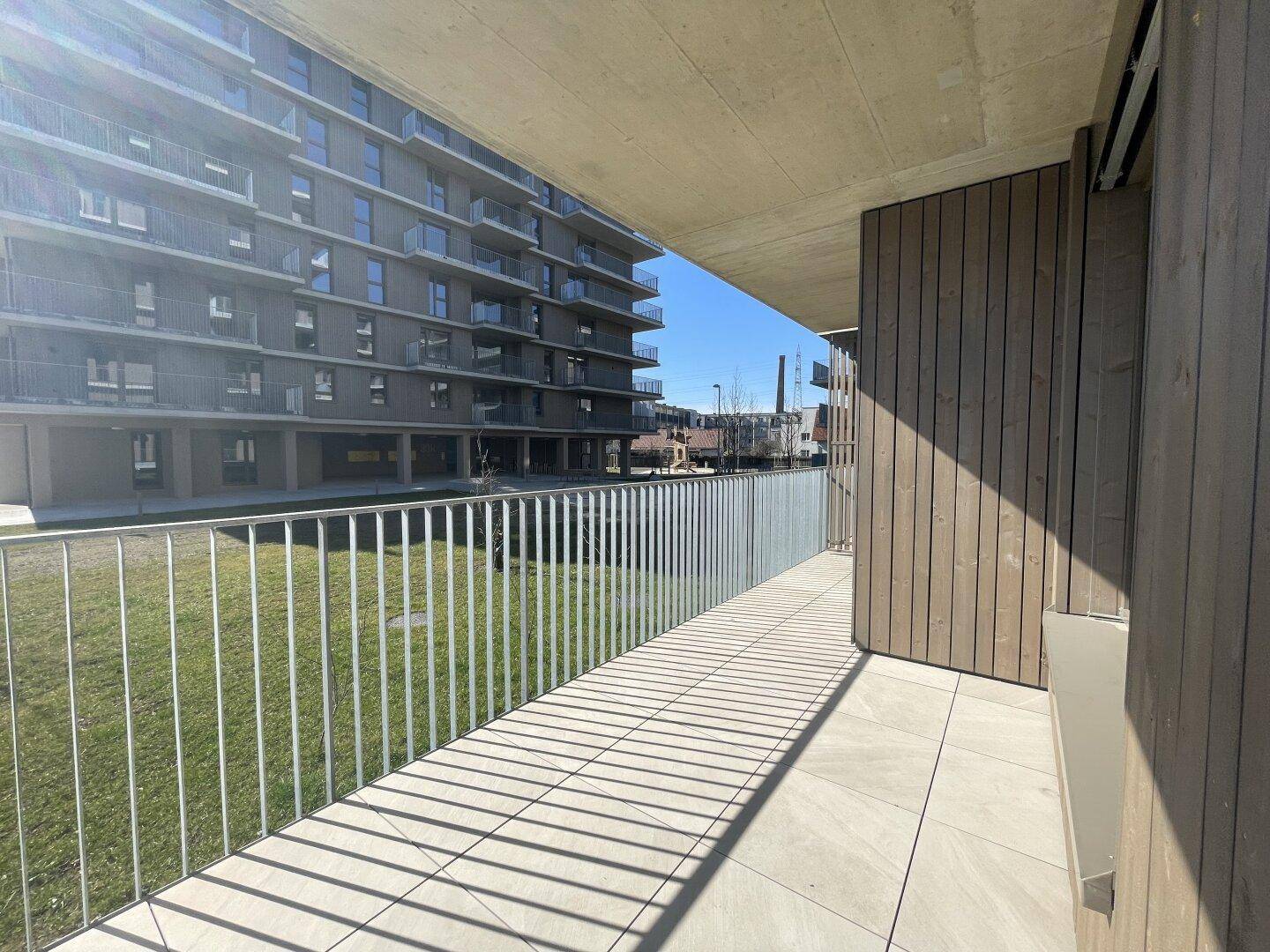 Langer Balkon mit Blick auf eine Grünfläche und andere moderne Wohngebäude, ideal zum Entspannen.