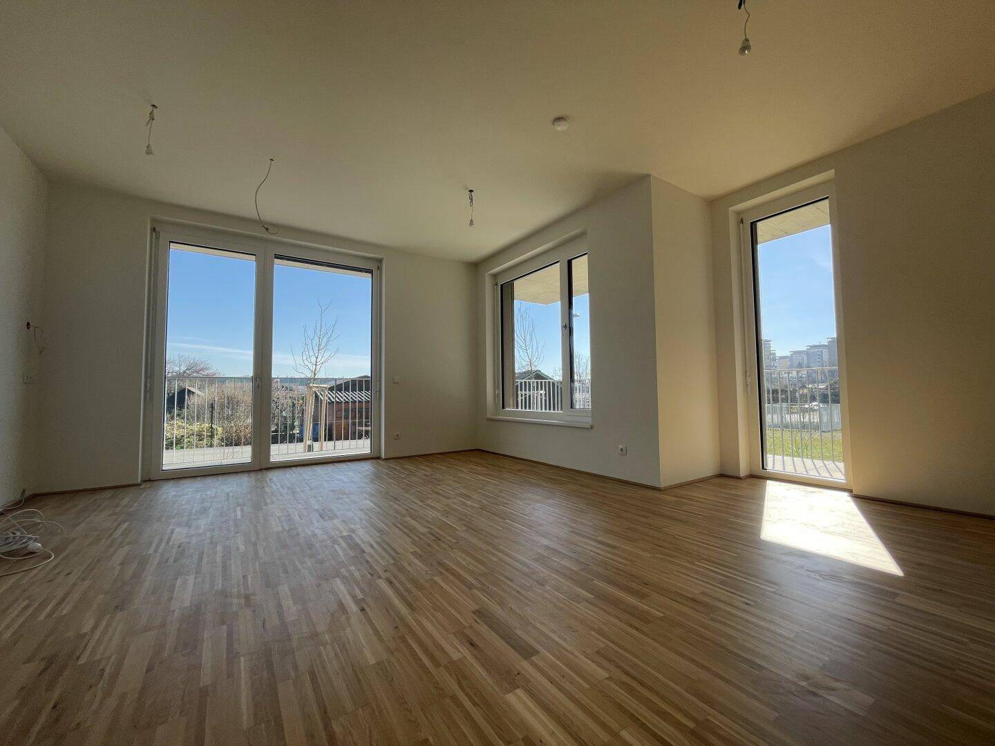 Heller Wohnbereich mit Parkettboden und großen Fenstern, die viel Tageslicht hereinlassen.