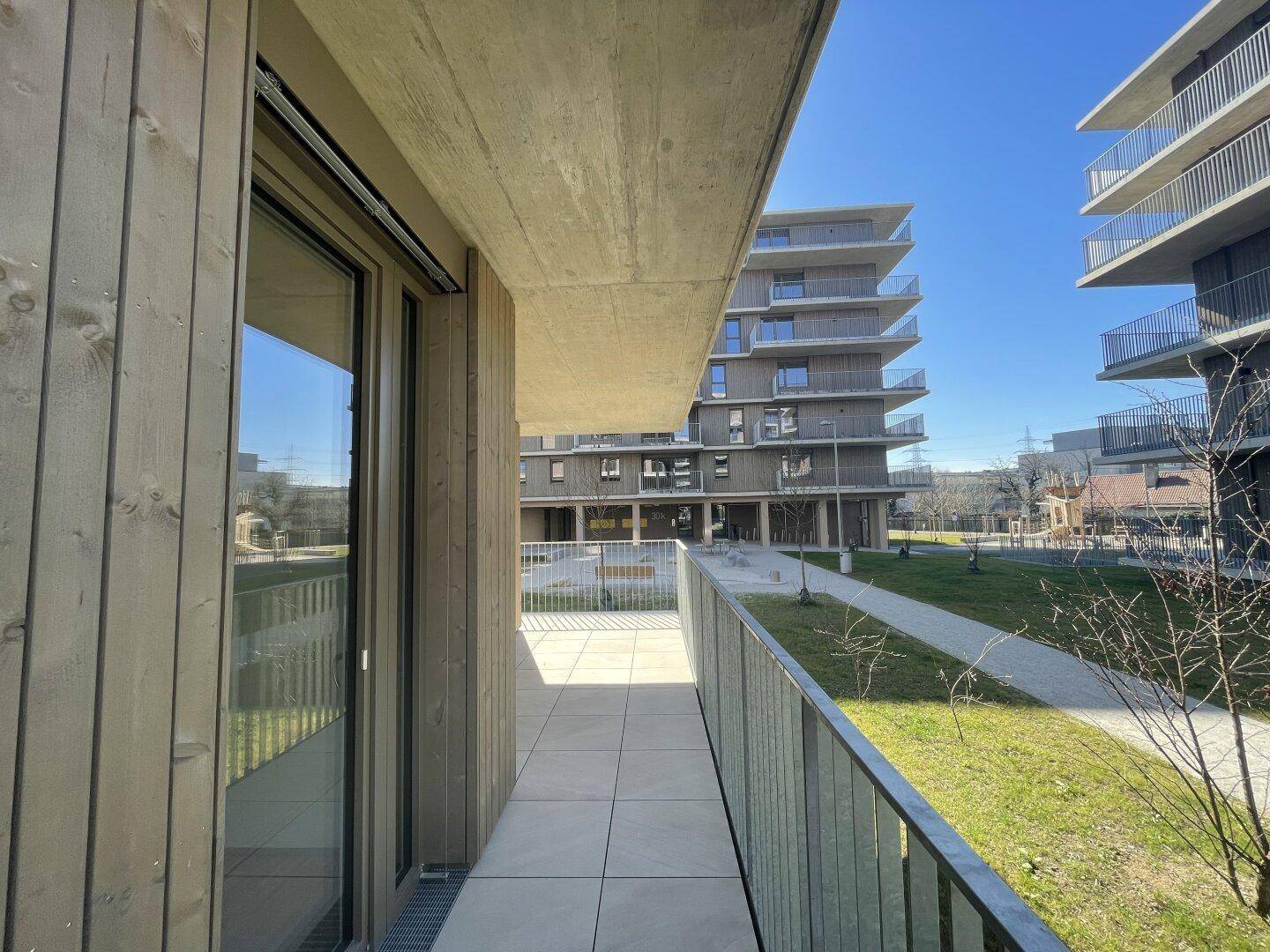 Heller Balkon mit Fliesenboden und Blick auf die grüne Umgebung und weitere Gebäude.