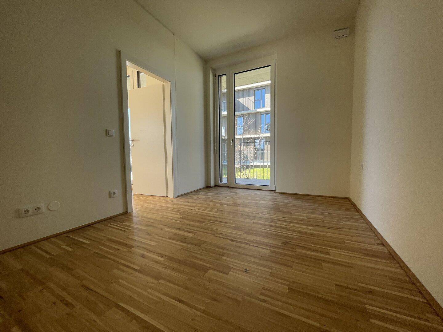 Helles Zimmer mit Holzboden und Zugang zu einem französischen Balkon oder einer kleinen Terrasse.