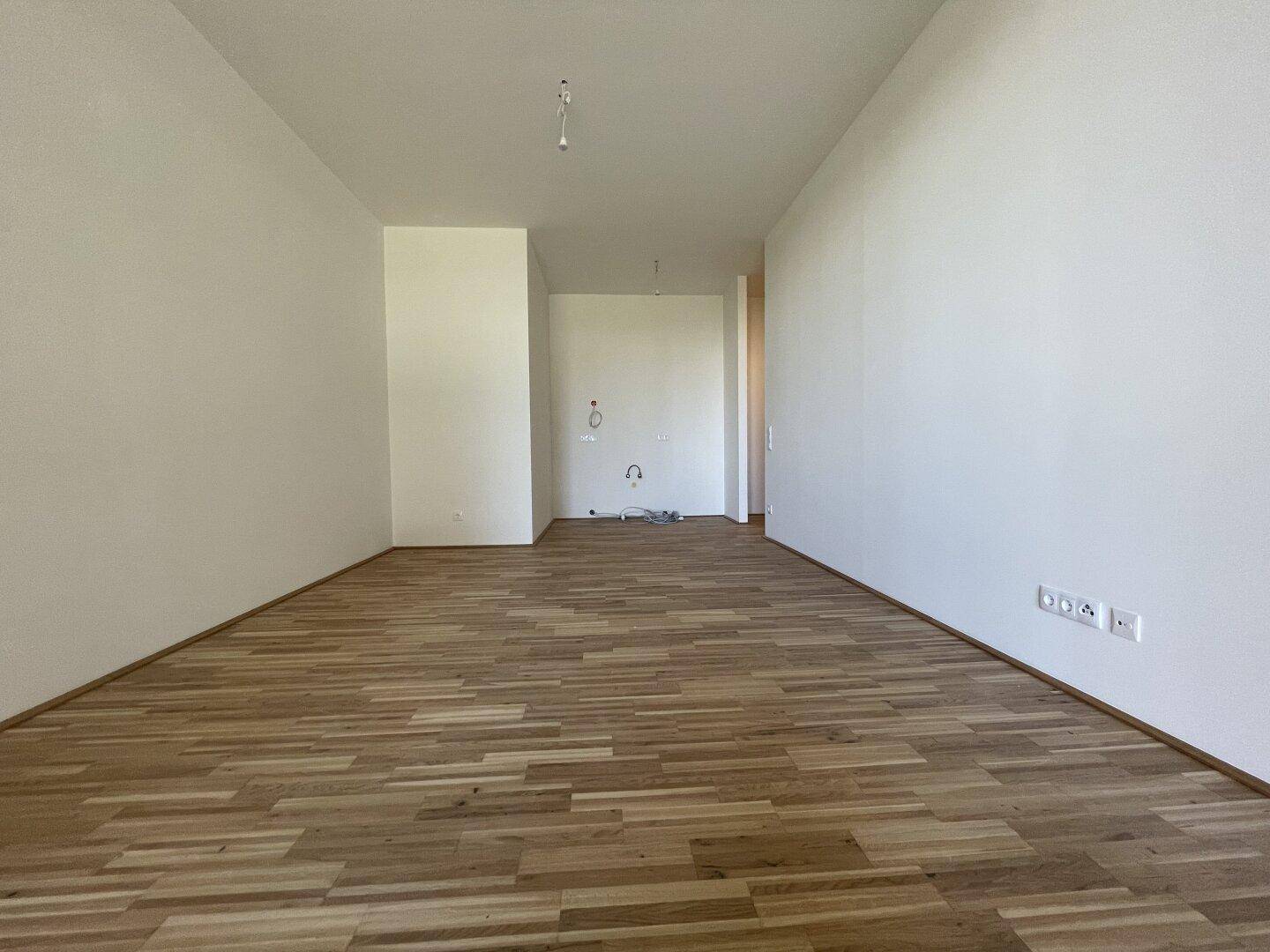 Geräumiger, leerer Raum mit hellem Holzparkett und weißen Wänden, bereit für die Einrichtung.