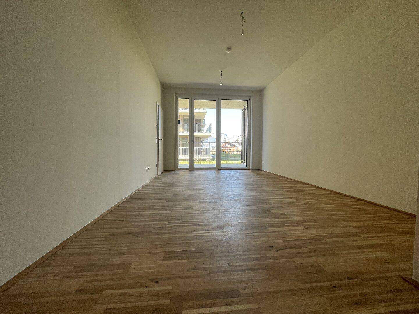 Heller Wohnraum mit Holzparkett und großen Glasfronten, die Zugang zum Außenbereich bieten.