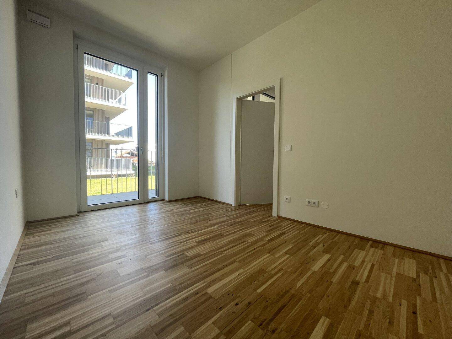Helles Schlafzimmer mit Holzparkett und Zugang zu einem Balkon oder einer Terrasse.