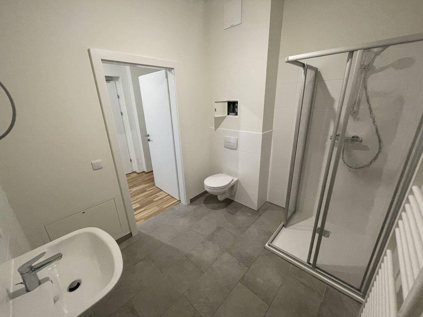 Modernes Badezimmer mit Dusche, WC, Waschbecken und grauen Fliesen.