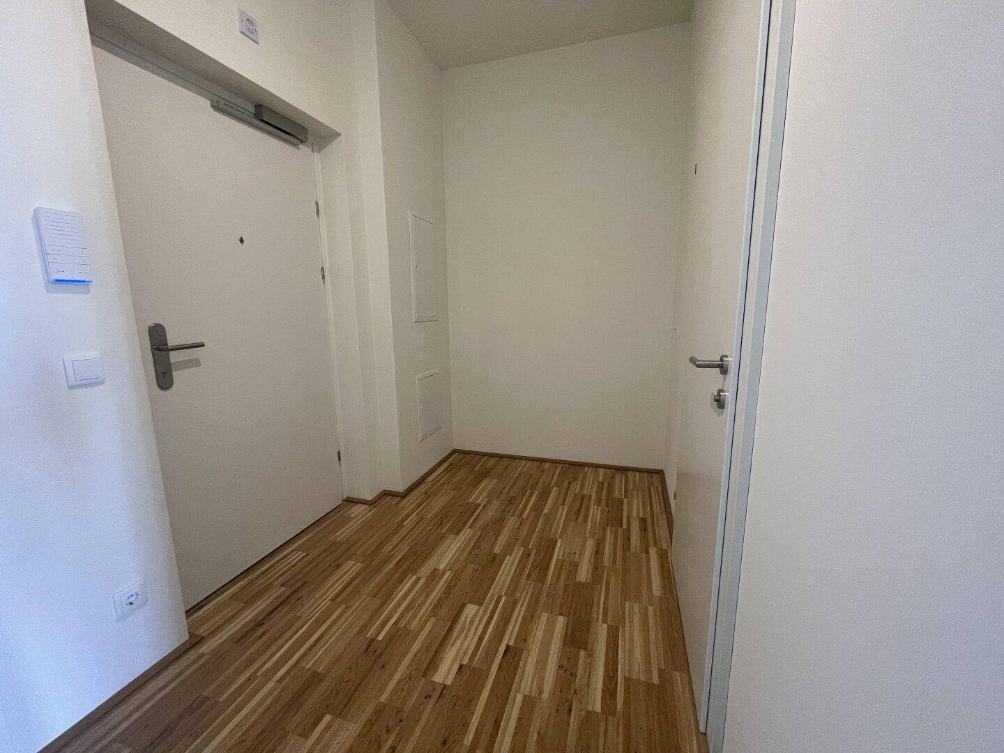 Eingangsbereich mit hellem Holzparkett und weißen Türen, der zu den Wohnräumen führt.