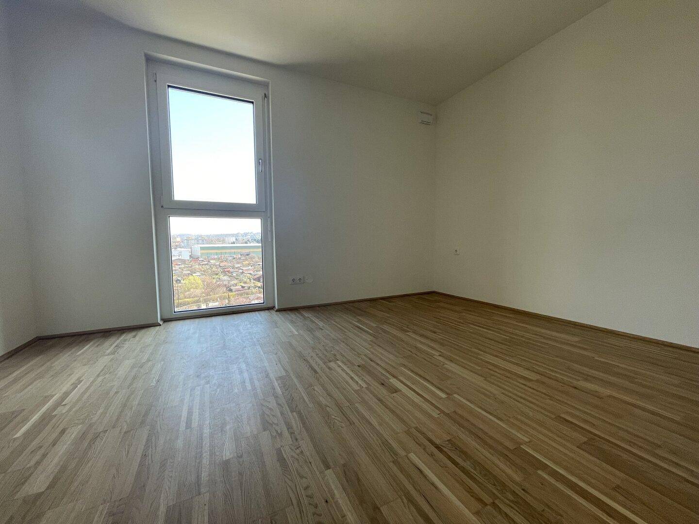 Helles Schlafzimmer mit Parkettboden und weitem Ausblick, bereit für individuelle Gestaltung.