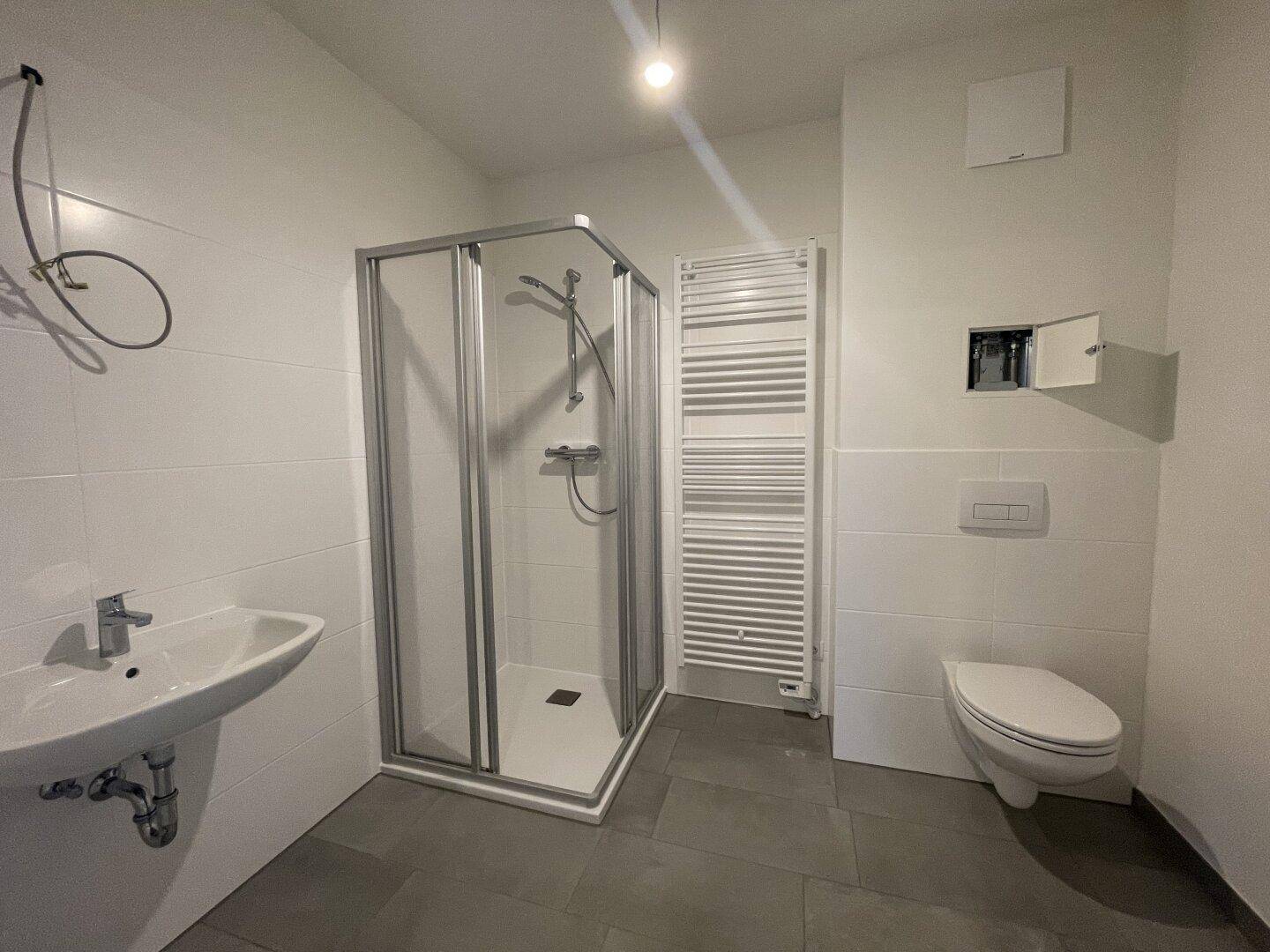 Modernes Badezimmer mit Dusche, WC, Waschbecken und beheiztem Handtuchhalter in hellen Farben.