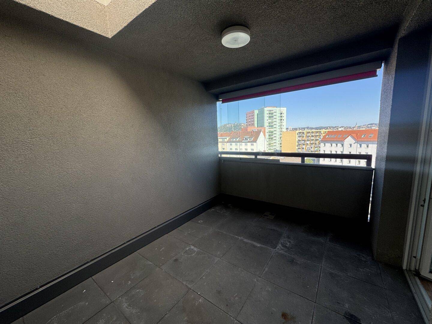 Überdachte Loggia mit dunklen Fliesen und Glasbrüstung, bietet einen urbanen Ausblick.