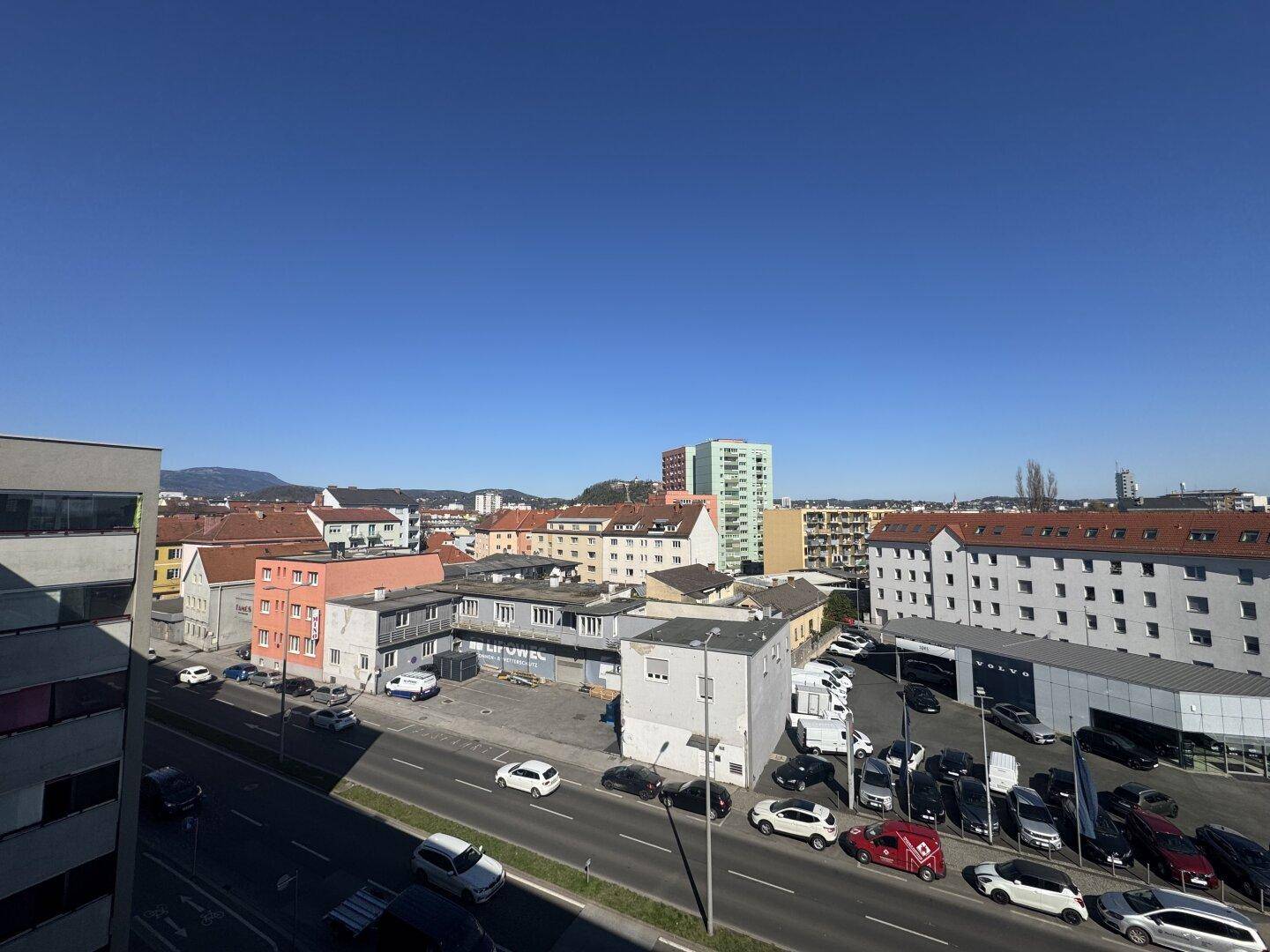 Weitläufiger Blick über eine städtische Straße mit Gebäuden und parkenden Autos.
