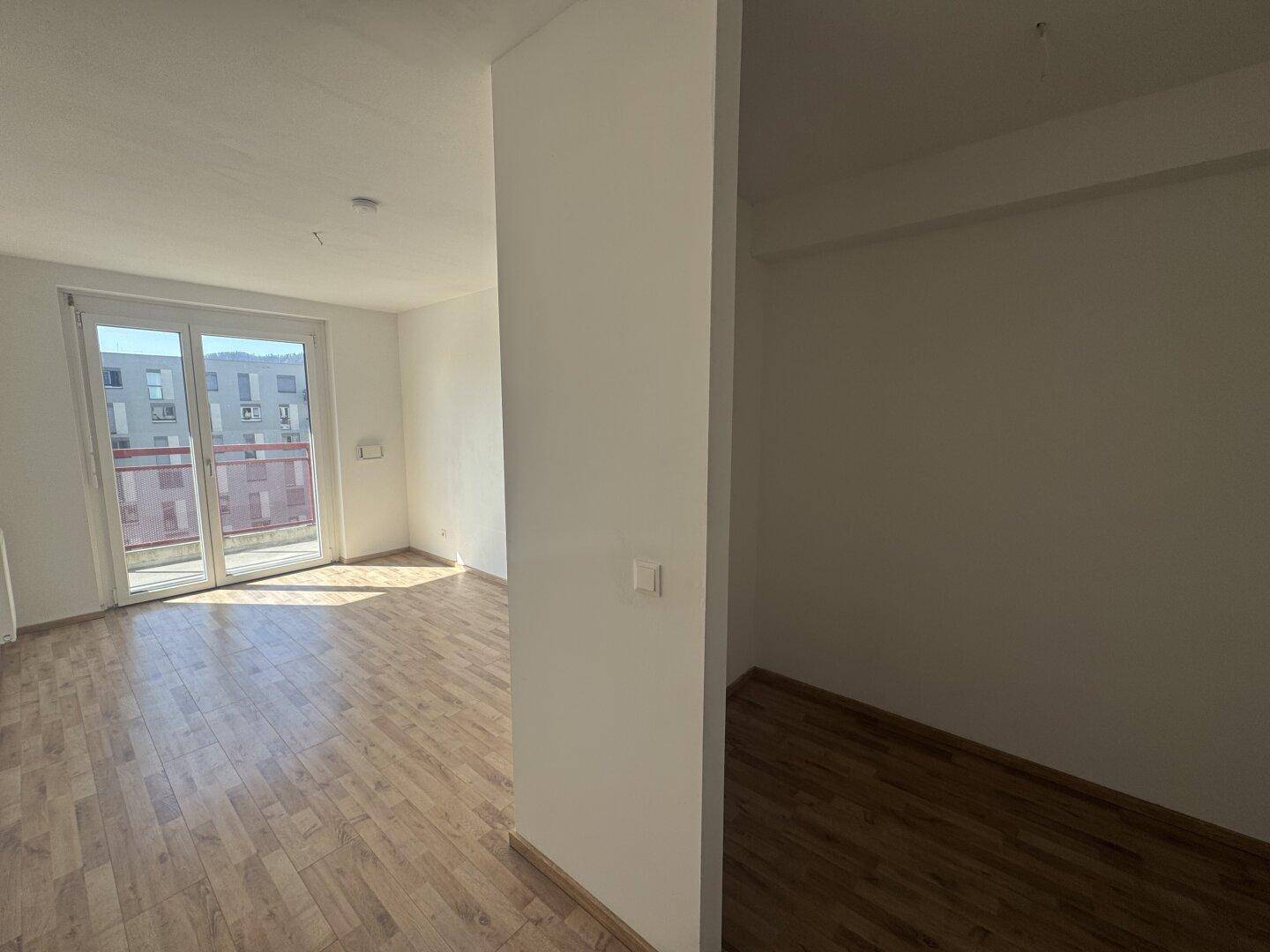 Heller Wohnraum mit Laminatboden und Zugang zu einem Balkon, inklusive einer kleinen Nische.