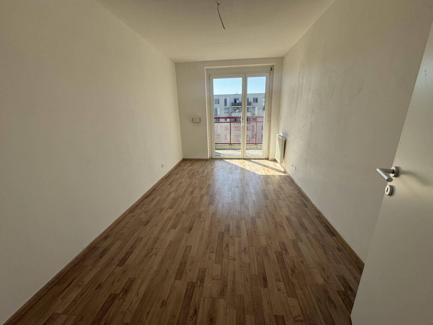 Helles Zimmer mit Laminatboden und Zugang zu einem Balkon, bietet viel natürliches Licht.