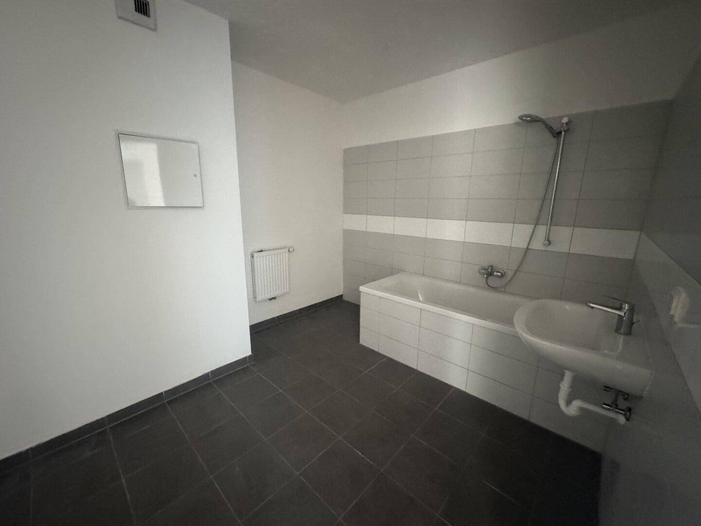 Badezimmer mit dunklen Bodenfliesen, hellgrauen Wandfliesen, Badewanne und Waschbecken.