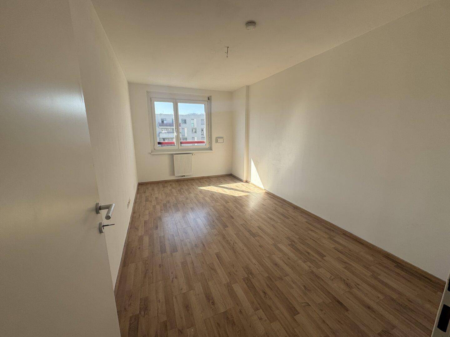 Helles Schlafzimmer mit Laminatboden und Fenster, das viel Sonnenlicht in den Raum lässt.