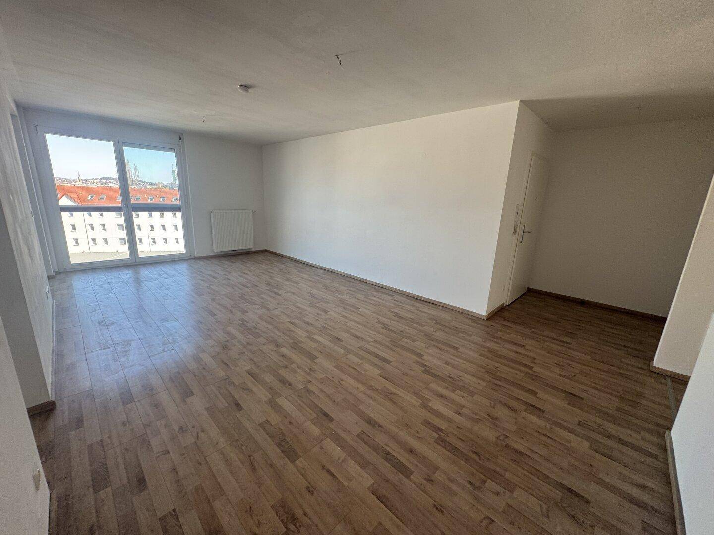 Geräumiges, helles Wohnzimmer mit Laminatboden und großen Fenstern, die den Raum erhellen.