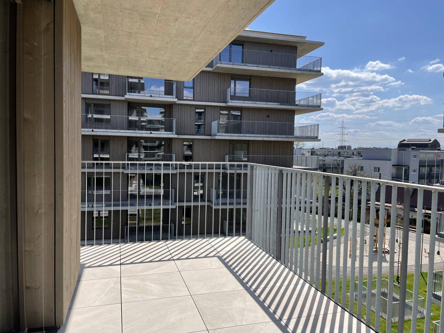 Sonniger Balkon mit Fliesenboden und Blick auf die umliegenden Neubauten und Grünflächen.