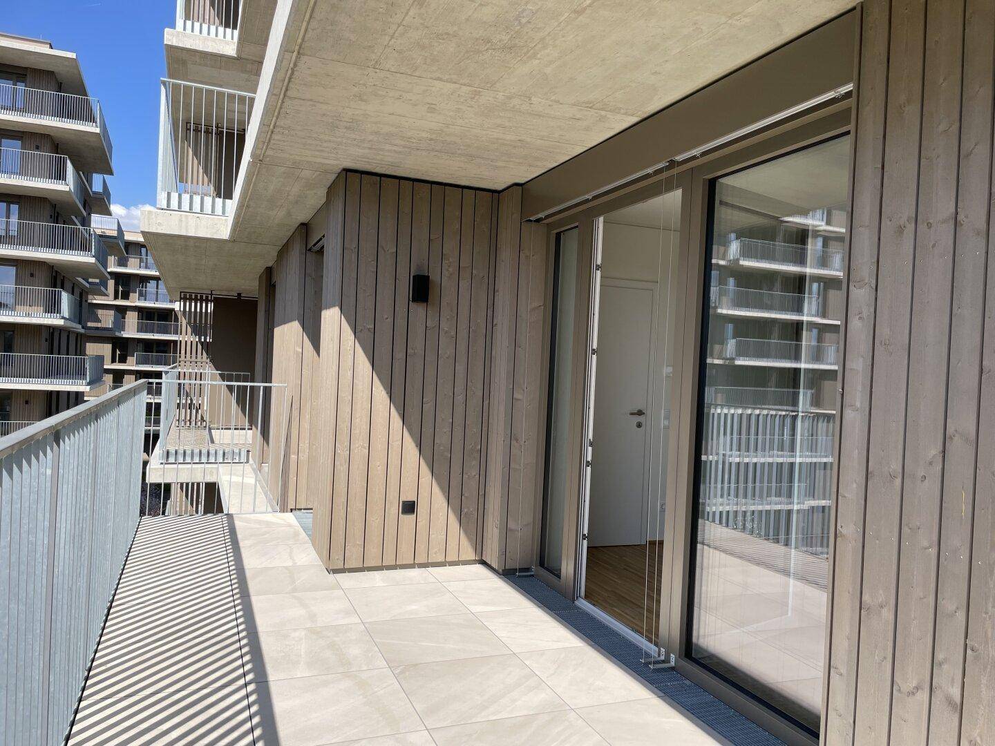 Heller Balkon mit Fliesenboden und Zugang zum Innenraum, umgeben von moderner Holzfassade.