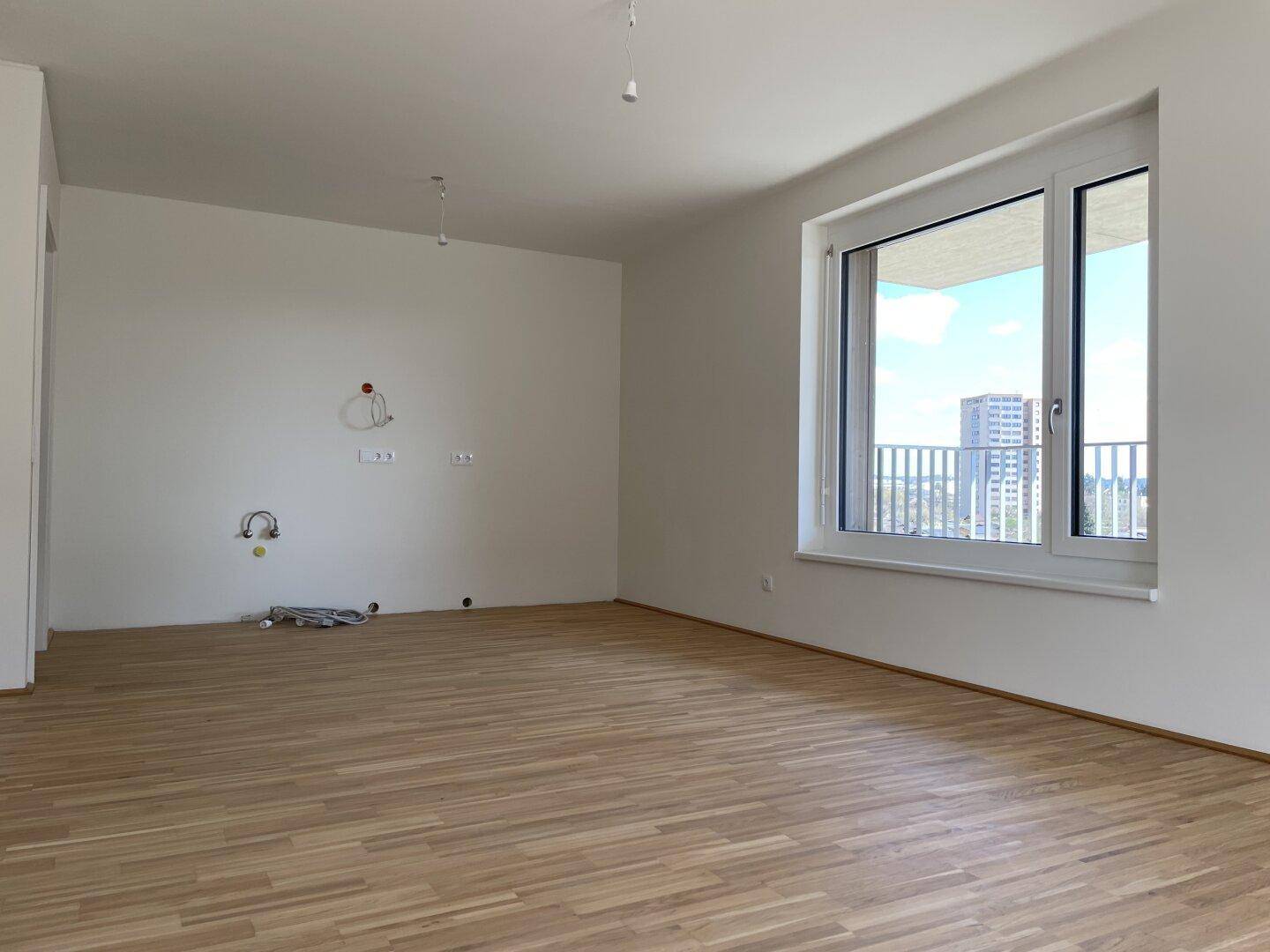 Leeres Wohnzimmer mit hellem Parkettboden und großem Fenster mit Stadtblick.