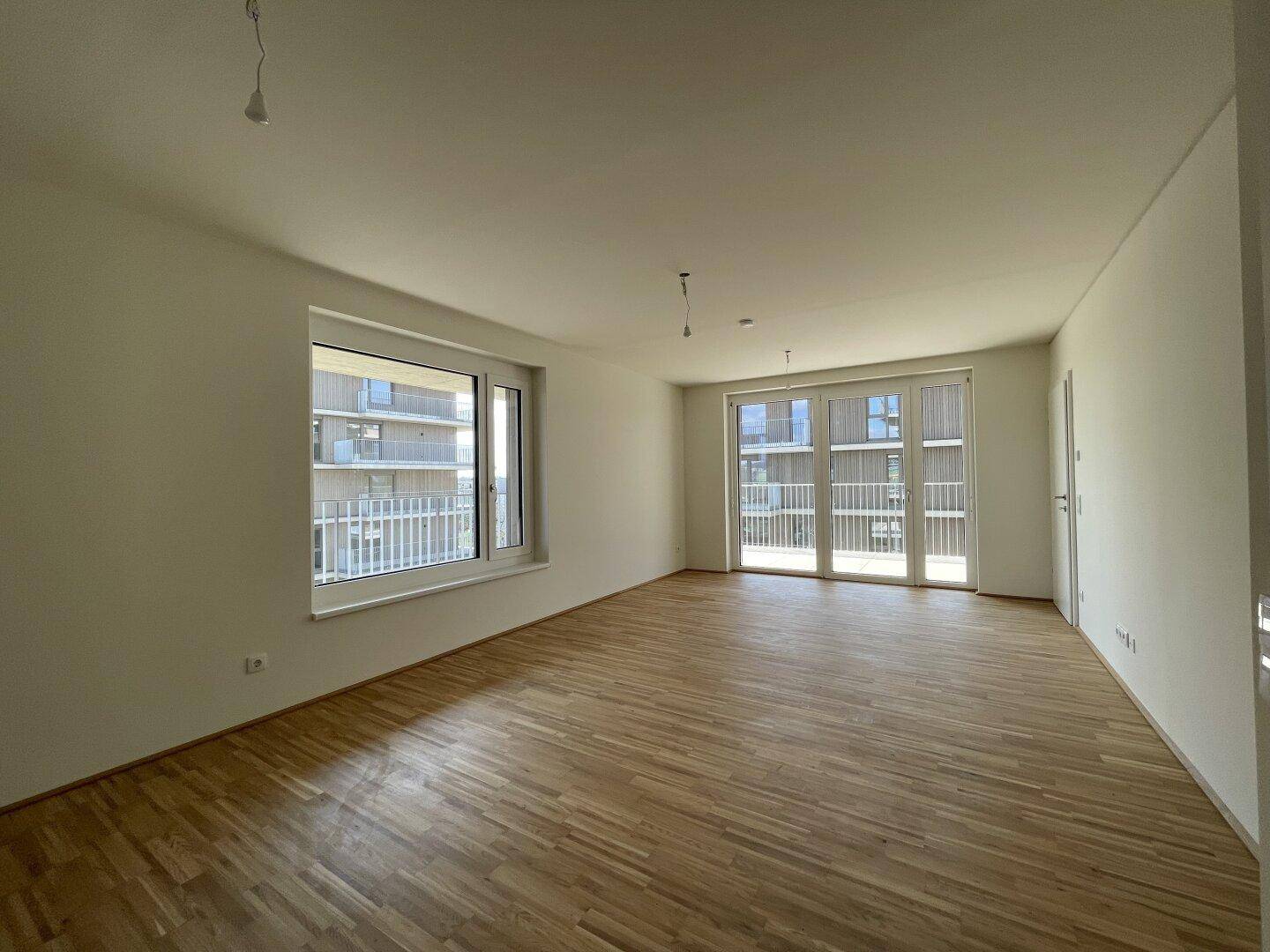 Helles Wohnzimmer mit Parkettboden und Zugang zu einem Balkon, ideal für offenes Wohnen.
