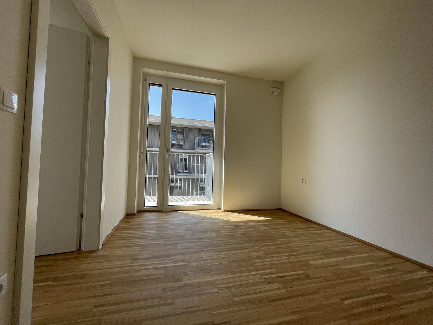 Helles Schlafzimmer mit Parkettboden und direktem Zugang zum Balkon, bereit zum Einrichten.