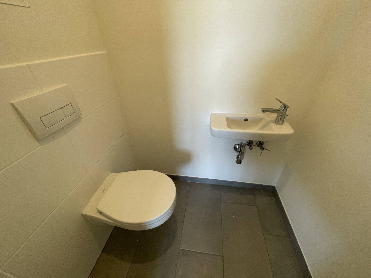 Modernes Gäste-WC mit wandhängender Toilette und kleinem Waschbecken, in neutralen Farben gehalten.