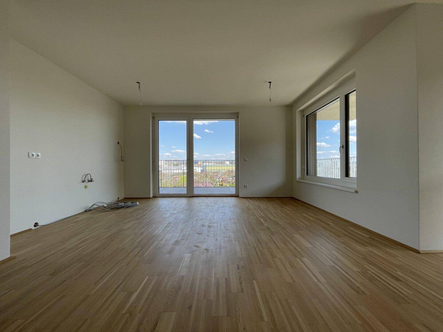 Geräumiges, unmöbliertes Wohnzimmer mit Holzboden und viel Tageslicht durch große Fenster.