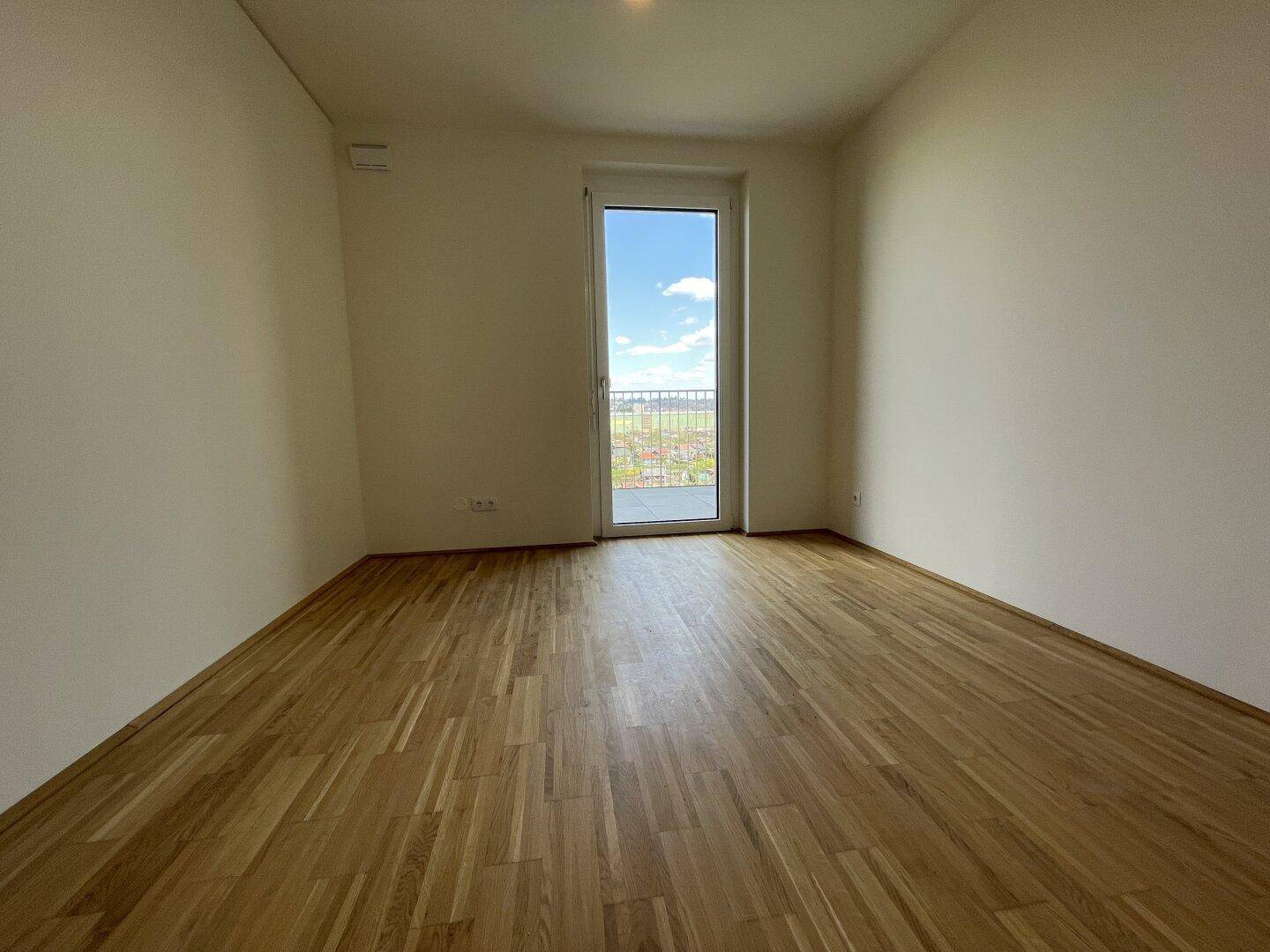 Leeres Schlafzimmer mit Parkettboden und Zugang zu einem französischen Balkon oder Fenster.